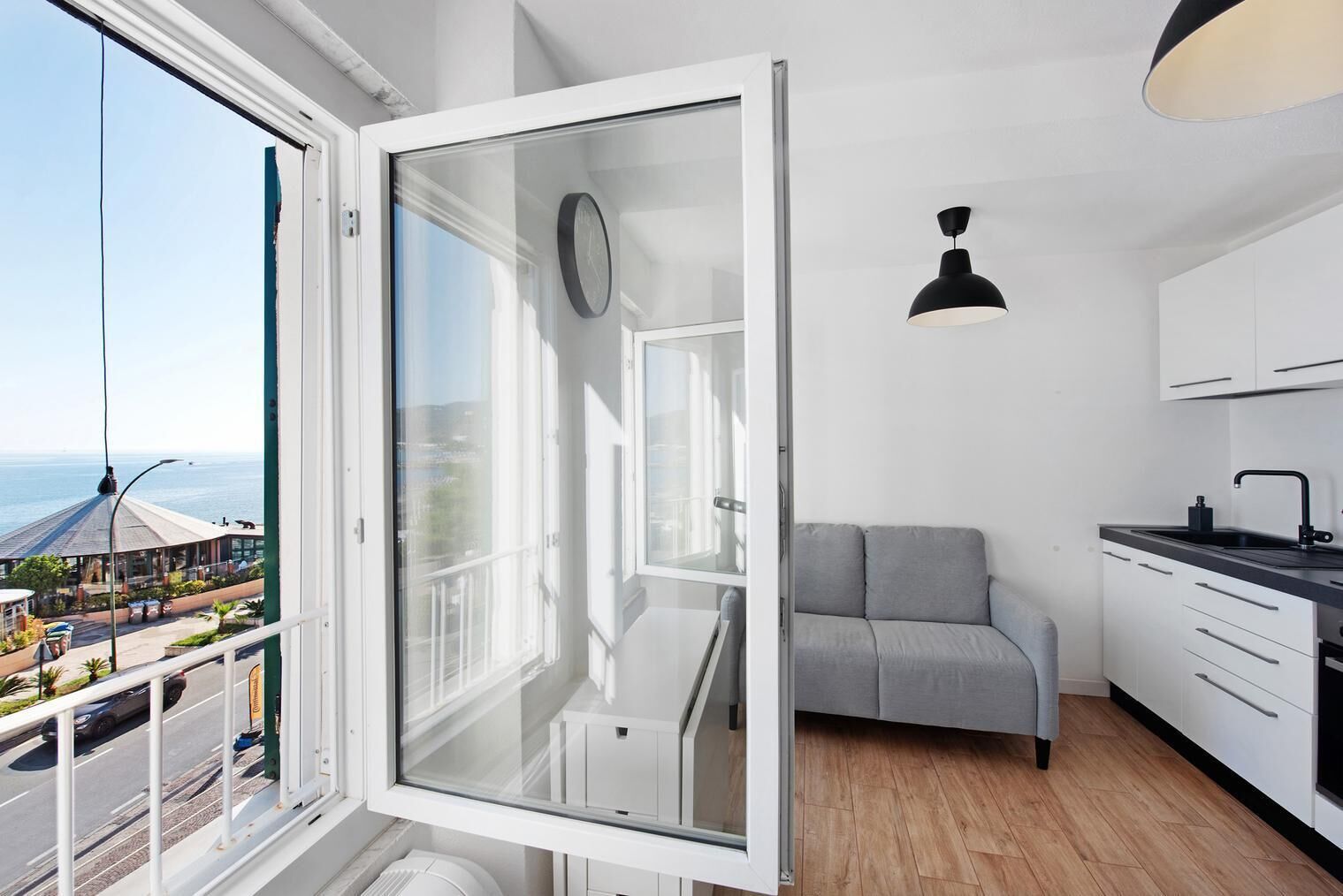 A modern kitchen with a grey sofa, a dining area, and a large window with a view of the sea.