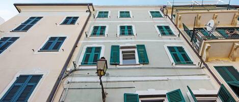 Un edificio de varios pisos con contraventanas verdes, una farola visible y un cielo despejado.