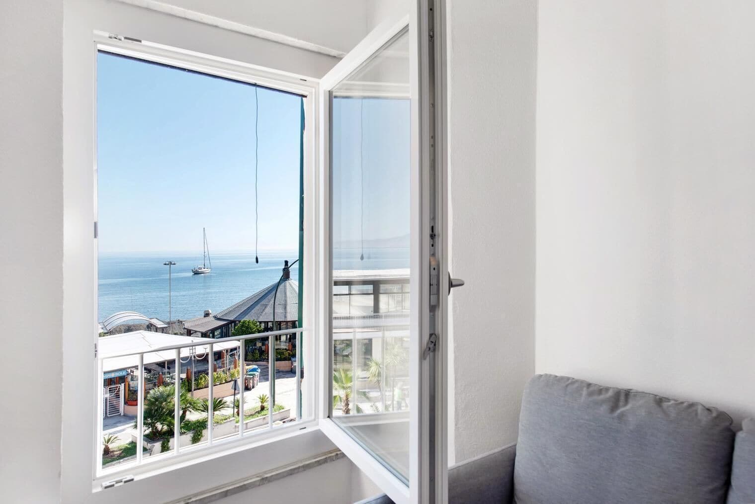 A room with a large window overlooking a marina with boats, a clear sky, and a view of buildings in the distance.