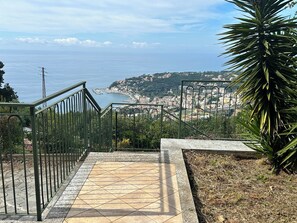 Eine Treppe führt zu einer Küstenansicht, im Hintergrund ist eine Stadt zu sehen.