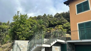 A stone staircase leading to a balcony with metal railings, a stone wall, and a building with green shutters.