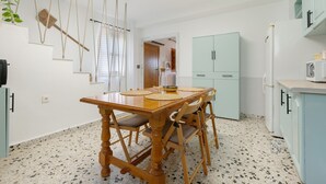 A dining area with a wooden table and chairs, a kitchen with light blue cabinets, and a hanging plant. - Holiday Home 'La Huerta Del Parral' with Wi-Fi and Air Conditioning (Soportújar)