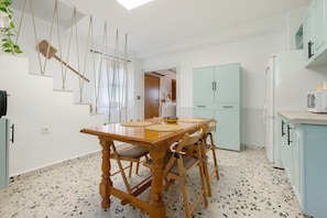 Un comedor con mesa y sillas de madera, una cocina con armarios azul claro y una planta colgante.