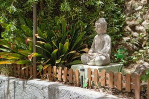 En Buddha-statue i en have med et træhegn, omgivet af grønt og sten.