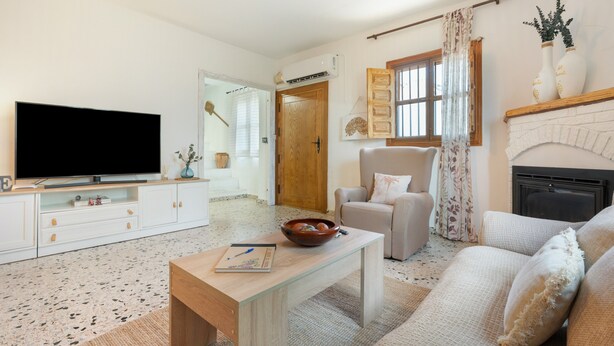 A living room with a flat-screen TV, a wooden coffee table, a beige sofa, a white armchair, and a fireplace. - Holiday Home 'La Huerta Del Parral' with Wi-Fi and Air Conditioning (Soportújar)