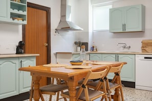 Una cocina con una mesa de madera, sillas, una cafetera y un lavavajillas.