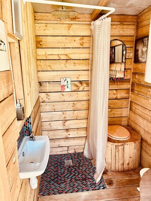 Une salle de bain rustique, aménagée dans une cabane en bois, avec un lavabo, des toilettes, un rideau de douche et un miroir.
