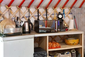 A kitchenette with a microwave, kettle, and coffee maker. There is a shelf with a yellow pot and a black bag. - Wellness Mongolian Yurt with Nordic Bath, All Comforts (Quimper)