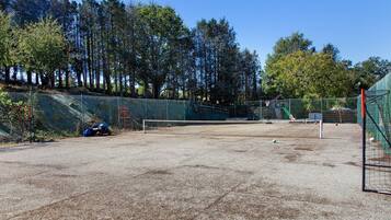 An outdoor tennis court with a net, surrounded by a fence and trees.