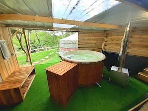 Une cabane en bois avec un jacuzzi, des bancs en bois et une vue sur la verdure.