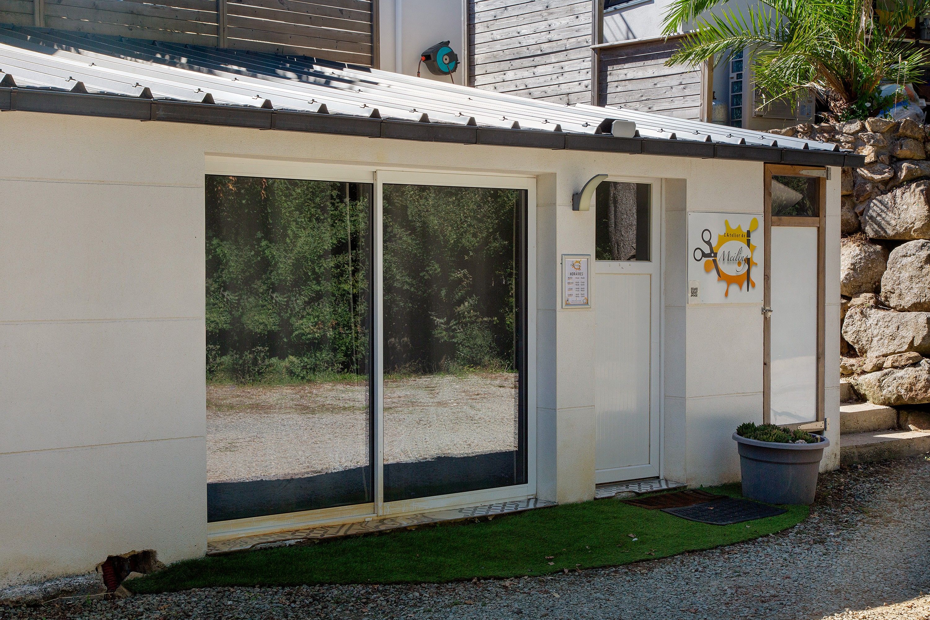 A building with a metal roof, a door with a glass panel, and a sign with a sun and scissors.