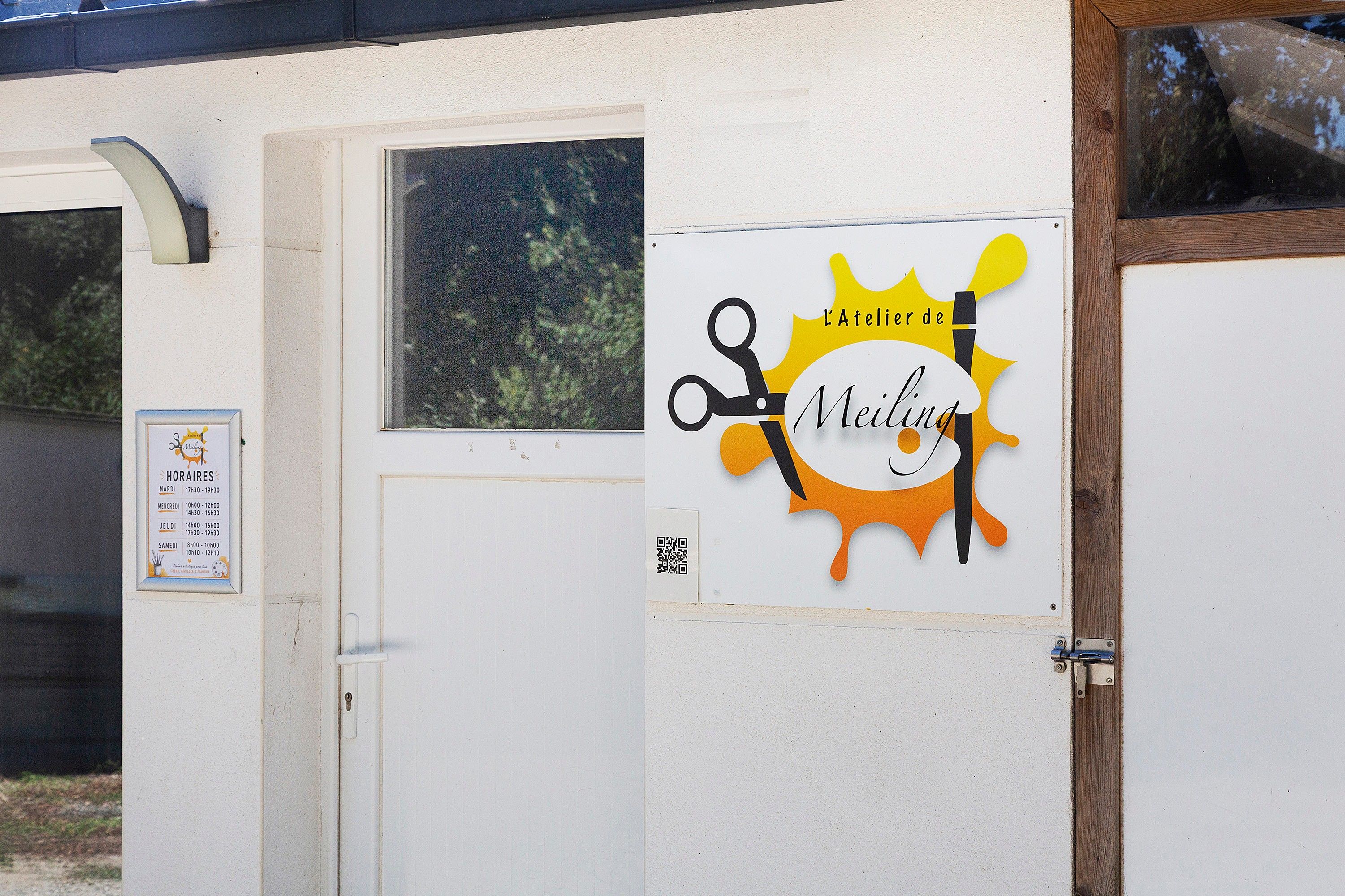 En dør med et skilt, der viser 'L'Atelier de Meiling', og en QR-kode.