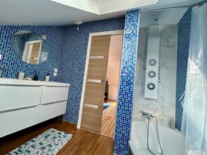 Een moderne badkamer met een blauwe mozaïektegelwand, een witte wastafel, een houten vloer en een badkuip met douchekop.