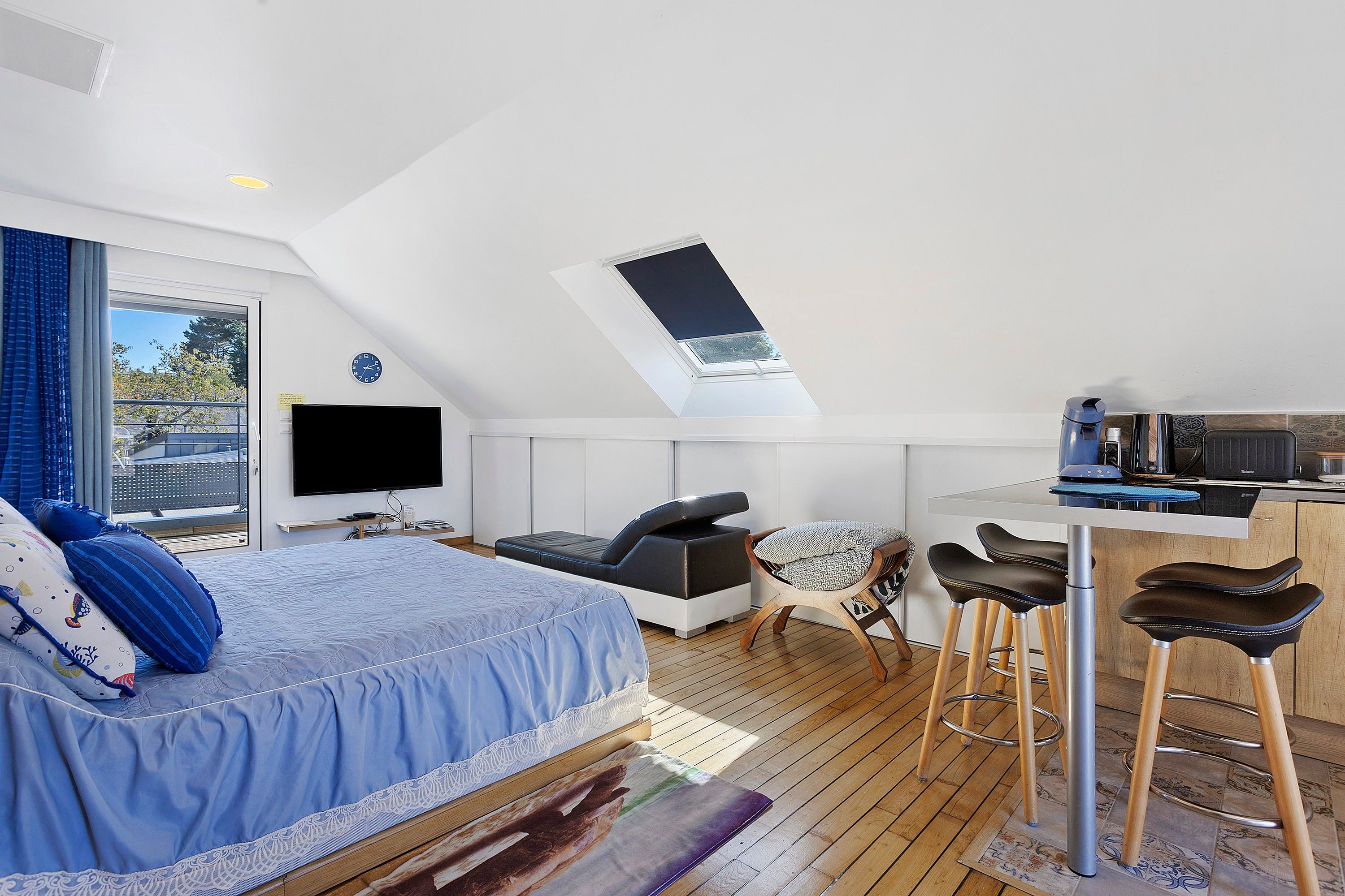 Ein modernes Schlafzimmer im Loft-Stil mit Dachfenster, einem großen Bett, einem Fernseher und einer Küchenzeile.