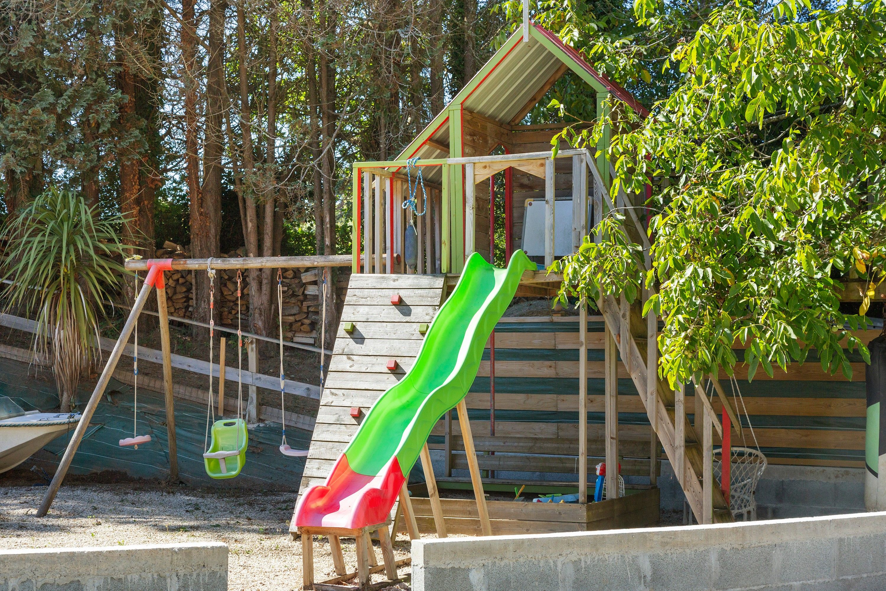 A playground with a slide, swings, and a small wooden structure.