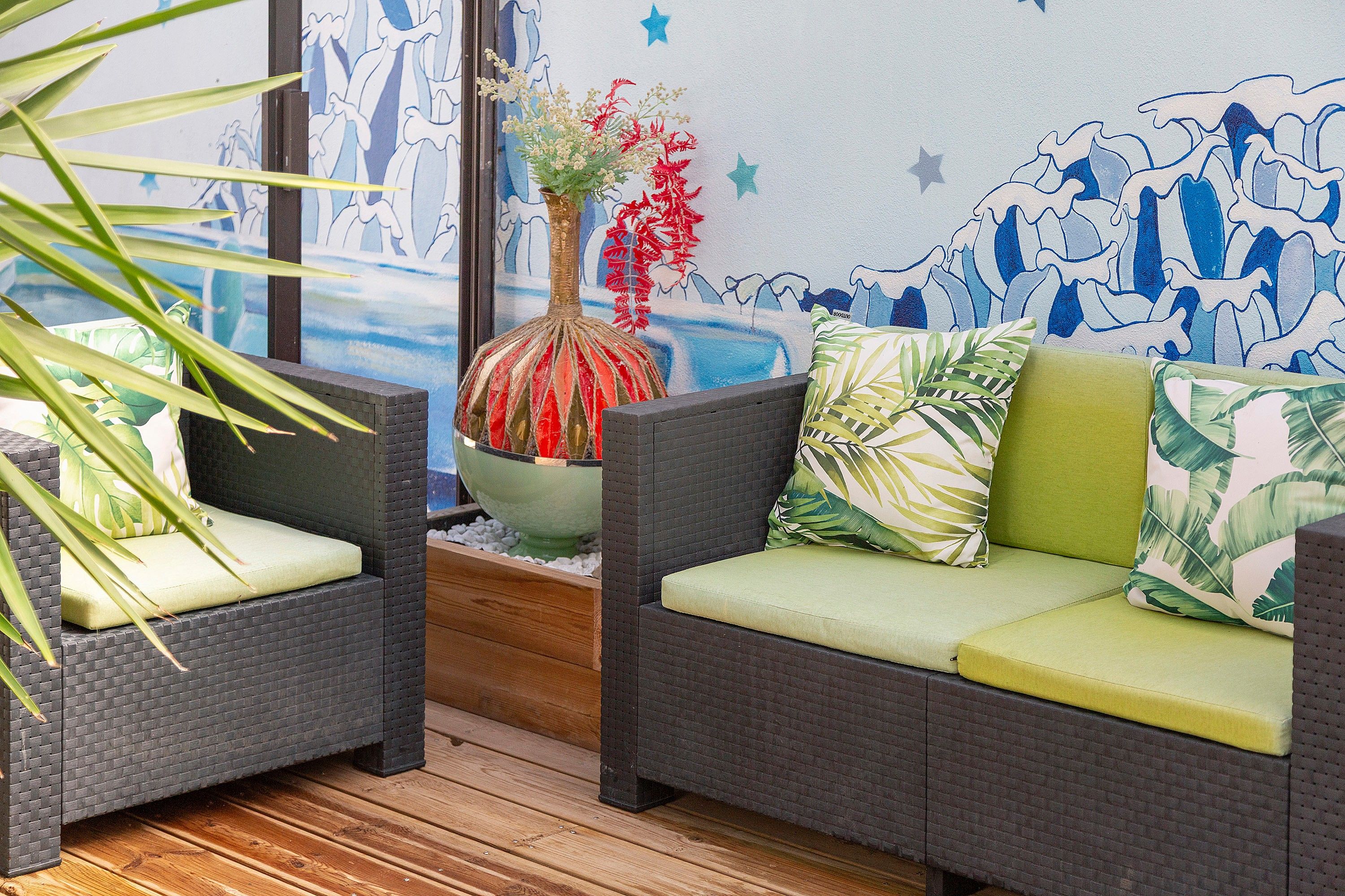 A room with wicker furniture, a green planter with red and white flowers, and a wall with a blue and white wave pattern.