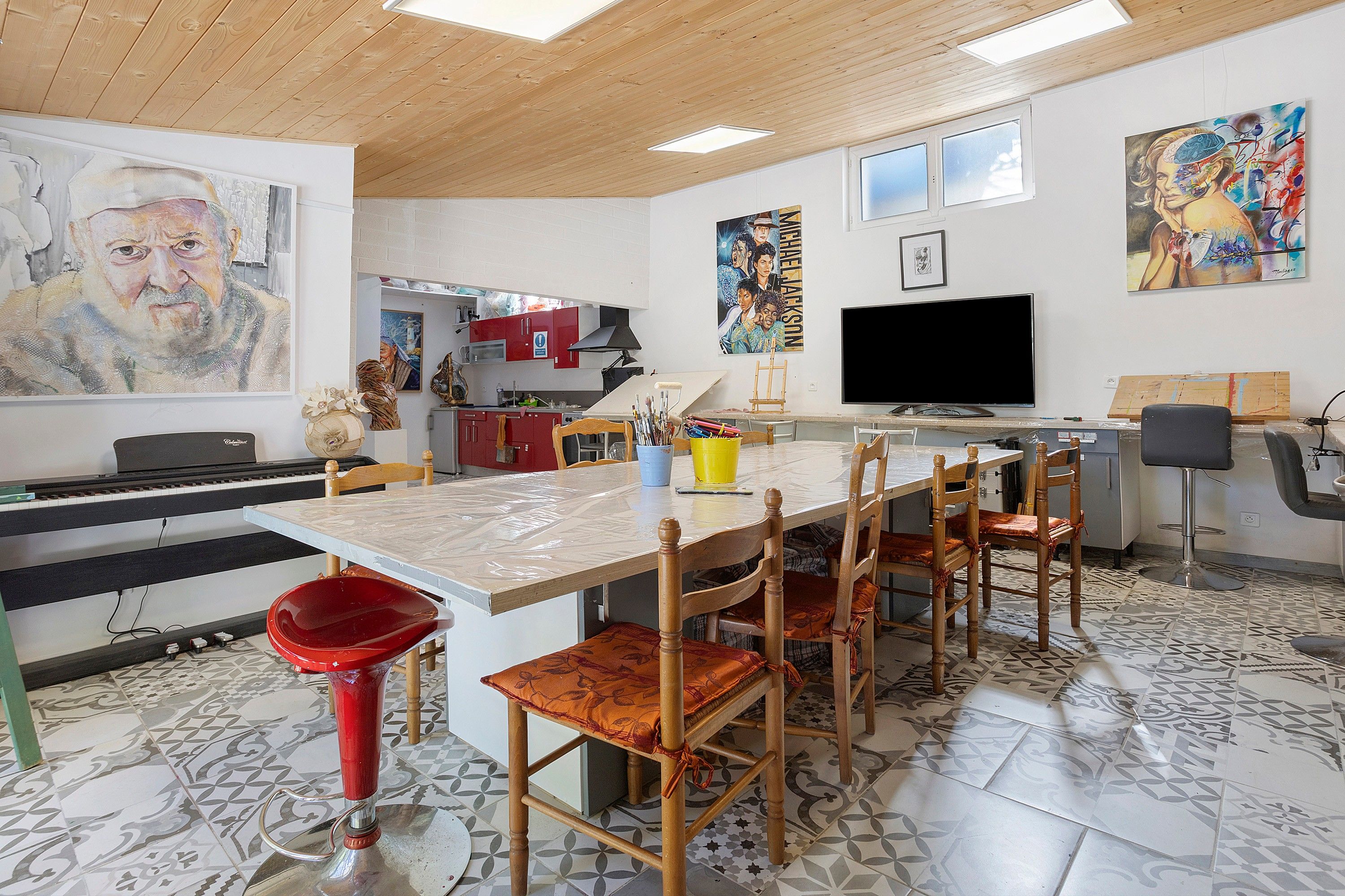 A spacious kitchen with a dining area, featuring a piano, a large painting, and a television.