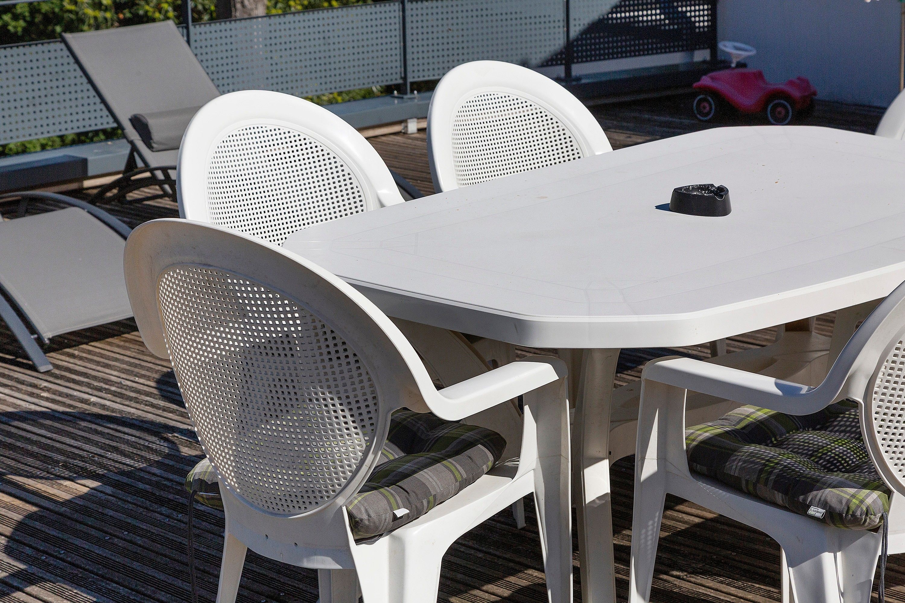 A white outdoor table with four chairs, each with a mesh backrest.