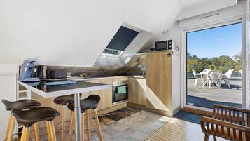 Cocina compacta con horno integrado, microondas y un pequeño comedor con taburetes.