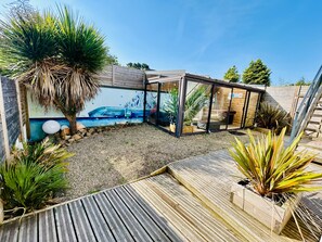 Een modern buitenzwembad met een houten terras, een lounge met glazen wanden en een muurschildering.