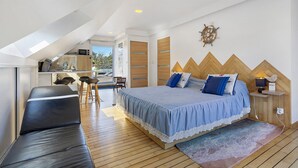 A modern bedroom with a loft-style ceiling, a bed with blue bedding, a wooden headboard, and a view of the outdoors. - In Nature – Spa – 2km from City Center (Quimper)