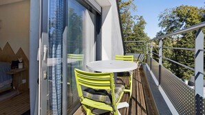 A balcony with a table and chairs, a sliding glass door, and a view of trees. - In Nature – Spa – 2km from City Center (Quimper)