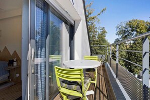 Een balkon met een tafel en stoelen, een schuifpui en uitzicht op bomen.