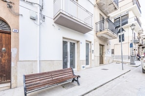 Un carrer amb una banca, un edifici amb balcons i un cartell de 'Millepini'.