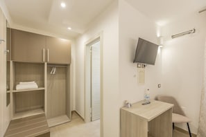 Habitació d'hotel amb un armari de fusta, escriptori, cadira, televisió penjada a la paret i zona de dutxa.