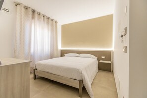 Un dormitori amb un llit, una taula de nit, una estora i un llum penjada a la paret.