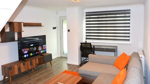 A modern living room with a flat-screen TV, a sofa, a coffee table, and a window with blinds. - Magic House- London (London)