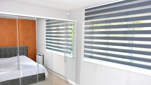A modern bedroom with a bed, a wardrobe, and a window with blinds. - Magic House- London (London)