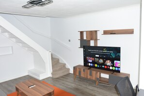 A modern living room with a staircase, a flat-screen TV, wooden furniture, and a carpeted floor. - Magic House- London (London)