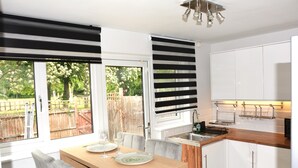 A modern kitchen with a dining area, large windows, and a view of the backyard. - Magic House- London (London)