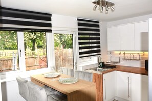 A modern kitchen with a dining area, large windows, and a view of the backyard. - Magic House- London (London)