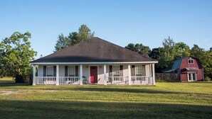 Ein Bungalow mit Veranda, einer roten Tür und einer kleinen angebauten Garage.