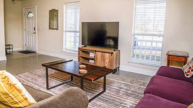 Ein Wohnzimmer mit einer Couch, einem Couchtisch, einem Fernseher auf einem Holzboden und zwei Jalousiewindern.
