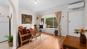 A modern living space with a sofa, a TV, a dining table, and a window with curtains. - Courtyard 2 Bed Apartment Mile End (Mile End)