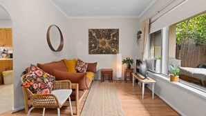 A living room with a sofa, a wicker chair, a coffee table, a TV, and a window with a view of greenery. - Courtyard 2 Bed Apartment Mile End (Mile End)