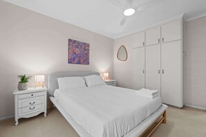 A bedroom with a bed, bedside tables, a wardrobe, a ceiling fan, and a wall art piece. - Courtyard 2 Bed Apartment Mile End (Mile End)