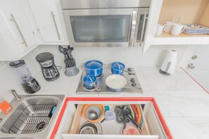Eine moderne Küche mit Mikrowelle aus Edelstahl, Kaffeemaschine und einer Auswahl an Töpfen und Pfannen.