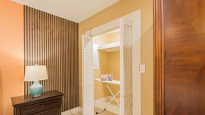 A hallway with a wooden dresser, a lamp, a closet with white shutters, and a wooden wardrobe. - The Master Suite / King Size Bed /Walk in Shower (McAllen)