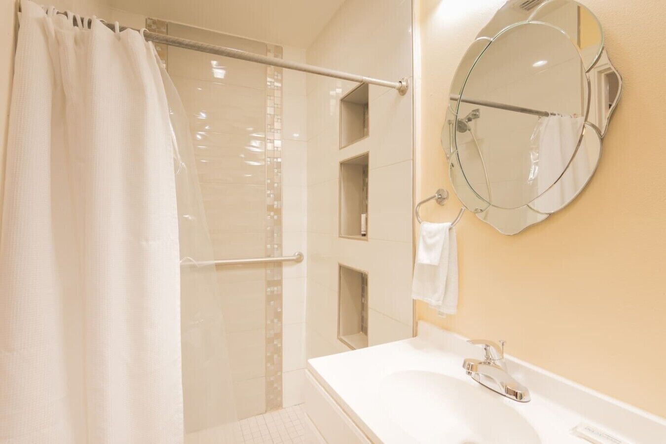 A bathroom with a shower, a sink, a mirror, and a towel rack.