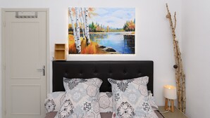 Une chambre à coucher avec un lit, des oreillers, une table de chevet, une lampe, un tableau et une porte.
