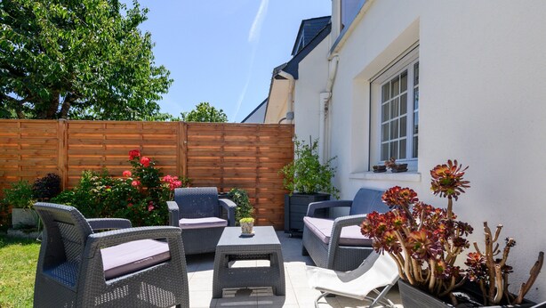 Une terrasse extérieure aménagée avec des meubles en osier, une petite table et des plantes en pot.