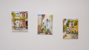 Trois tableaux représentant une charmante rue de village, avec des bâtiments, un pont et des plantes en pot.
