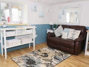 Ein Zimmer mit einem braunen Ledersofa, einem weißen Konsolentisch mit Körben, einem gemusterten Teppich und einem Spiegel an der Wand.