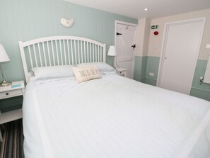 Ein ordentlich bezogenes Bett mit Kissen, ein Nachttisch mit Lampe und eine Tür mit Notausgangsschild.