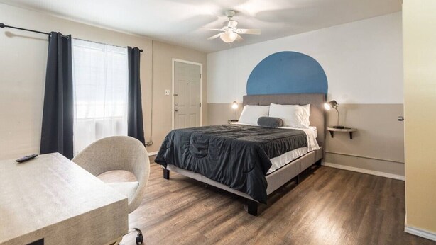 Quarto de hotel com cama, escrivaninha, cadeira, ventoinha de teto e porta.