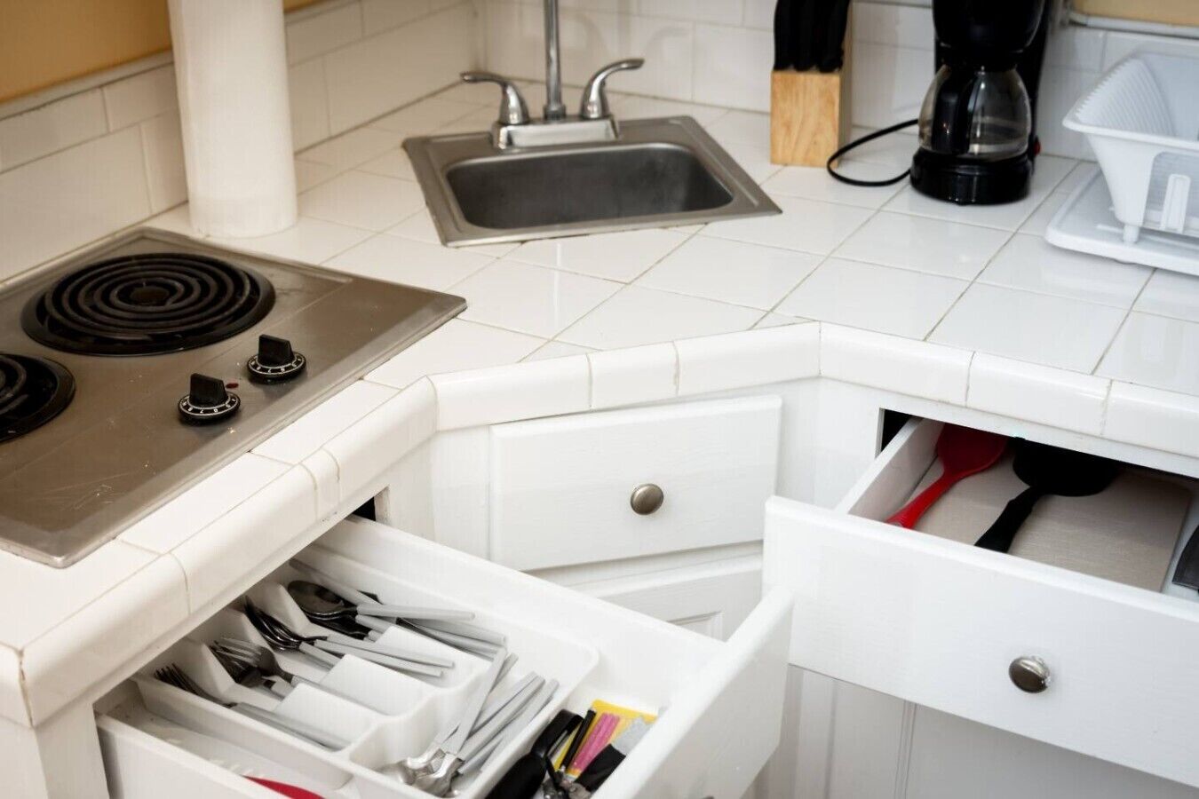 Una cucina con piano cottura, lavello e cassetti pieni di utensili.